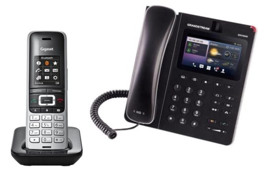 Telefon bezprzewodowy Gigaset w czarno-srebrnej obudowie na podstawce oraz czarny telefon stacjonarny Grandstream GXV3240 z kolorowym wyświetlaczem i słuchawką przewodową.